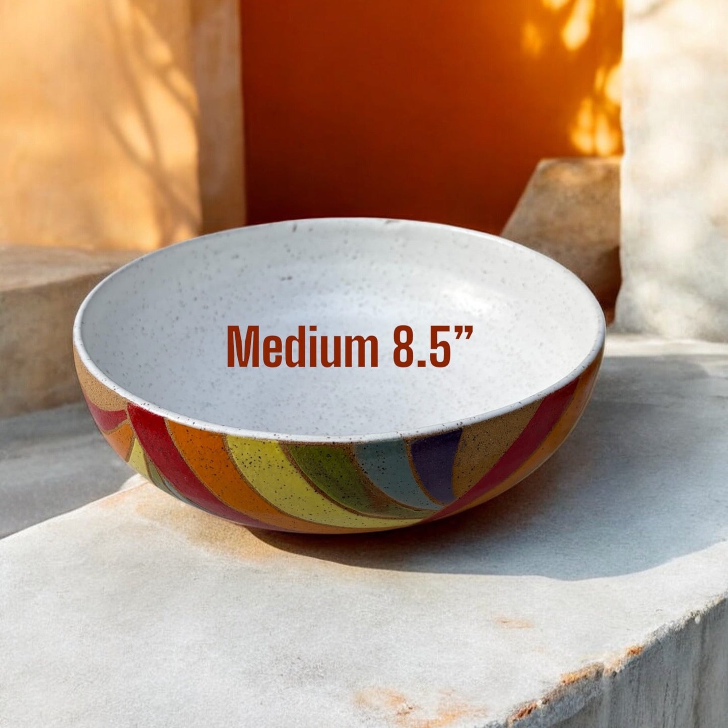 Colorful bowl with 'Medium 8.5”' text on a stone surface with a warm background